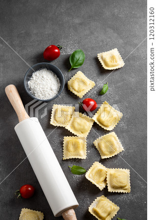 Flat lay of pasta ravioli with tomato and basil on dark background with flour and rolling pin. Flat lay of pasta ravioli with tomato and basil on dark background with flour and rolling pin. 120312160