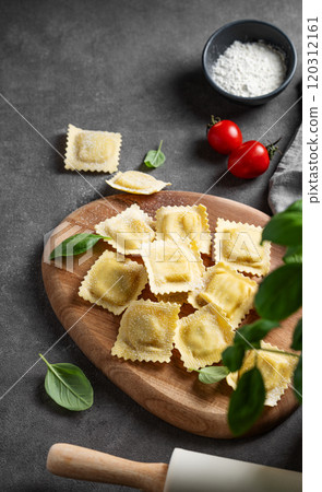 Flat lay of pasta ravioli with tomato and basil on wooden board on dark background with flour Flat lay of pasta ravioli with tomato and basil on wooden board on dark background with flour 120312161