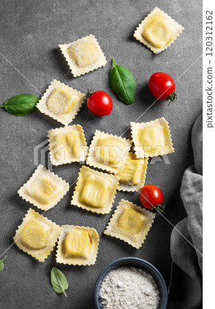 Flat lay of pasta ravioli with tomato and basil on dark background with flour and napkin. 120312162