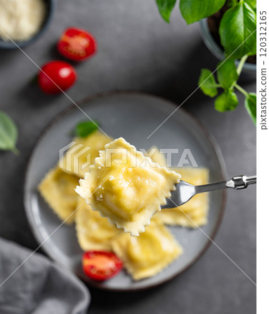 Homemade ravioli pasta with cheese, tomatoes and basil in a plate on a dark background with napkin Homemade ravioli pasta with cheese, tomatoes and basil in a plate on a dark background with napkin 120312165