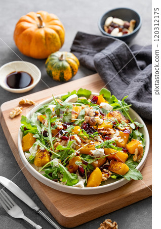 Autumn salad with pumpkin, arugula, feta cheese, nuts and dried berries in a plate  120312175