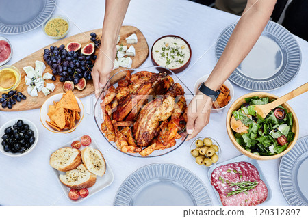 Top view of male hands putting delicious roasted chicken dish on festive dinner table outdoors with white cloth copy space 120312897