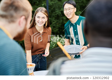 Group of cheerful adult friends setting table together outdoors preparing for dinner party Group of cheerful adult friends setting table together outdoors preparing for dinner party 120312902