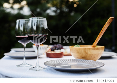 Close up background image of beautiful dining table setting outdoors with focus on two glasses with red wine copy space 120312904