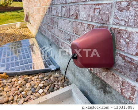 A red exterior vent cover on a brick wall, with a custom plexiglass window well cover surrounded by decorative rocks in a landscaped backyard during the late fall season. A red exterior vent cover on a brick wall, with a custom plexiglass window well cover surrounded by decorative rocks in a landscaped backyard during the late fall season. 120313093