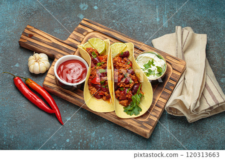 Mexican tacos with chili con carne, red beans, and lime wedges on wooden board top view 120313663