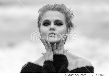 Woman with short hair and makeup is striking pose on natural background. Fashion model playfully put both palms on neck, looks so confident and looking at camera. Black and white dramatic portrait 120314666