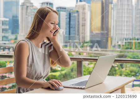 Young woman is working on a laptop on her balcony overlooking the skyscrapers. Freelancer, remote work, work from home Young woman is working on a laptop on her balcony overlooking the skyscrapers. Freelancer, remote work, work from home 120315690