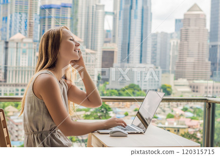 Young woman is working on a laptop on her balcony overlooking the skyscrapers. Freelancer, remote work, work from home 120315715