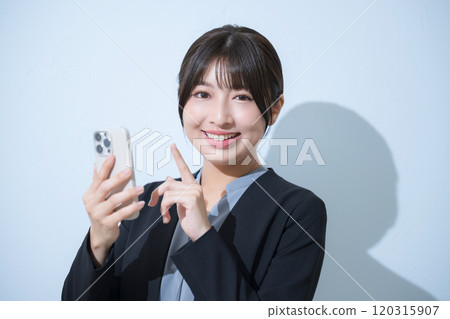 一位身穿西裝的年輕女子一邊打電話一邊看著鏡頭，同時敲擊淺藍色背景的商業場景 120315907