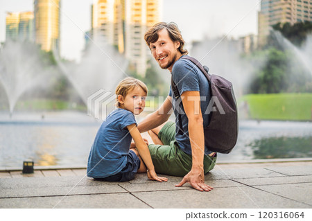 Dad and son tourists on background of fountain on the lake at night, near by Twin Towers with city on background. Kuala Lumpur, Malaysia Dad and son tourists on background of fountain on the lake at night, near by Twin Towers with city on background. Kuala Lumpur, Malaysia 120316064