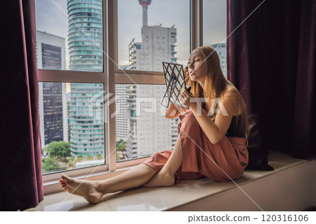 Young woman does makeup sitting by the window with a panoramic view of the skyscrapers and the big city 120316106