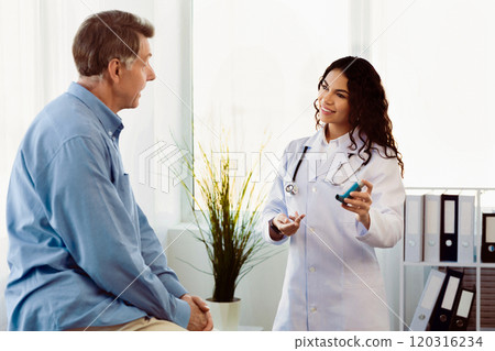 Healthcare Concept. Mexican doctor explaining how to use asthma inhaler to senior patient, empty space Healthcare Concept. Mexican doctor explaining how to use asthma inhaler to senior patient, empty space 120316234