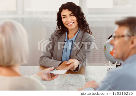 Tour Agency Concept. Smiling mexican female travel agent giving tickets to happy elderly couple, copyspace Tour Agency Concept. Smiling mexican female travel agent giving tickets to happy elderly couple, copyspace 120316250