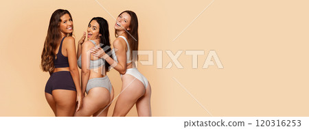 Three multiracial young women in stylish activewear smiling and posing playfully, exuding confidence and camaraderie, has fun on beige backdrop. Confidence, wellness, friendship, copy space Three multiracial young women in stylish activewear smiling and posing playfully, exuding confidence and camaraderie, has fun on beige backdrop. Confidence, wellness, friendship, copy space 120316253