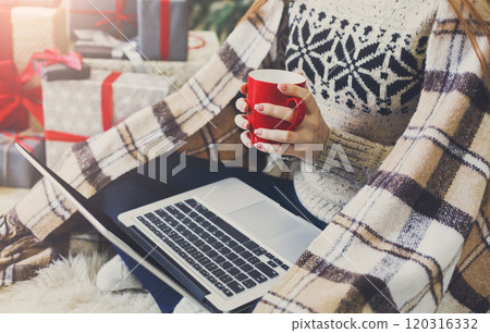 Christmas online shopping. Woman has coffee, buy presents on laptop, prepare to xmas, among gift boxes and packages. Winter sales 120316332