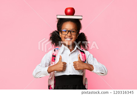 Happy Black Schoolgirl Holding Book And Apple On Head Gesturing Thumbs Up Posing On Yellow Background. Studio Shot 120316345