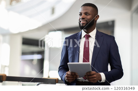 Cheerful young bearded african american man manager walking by office building corridor, holding modern digital tablet, using mobile app for business, looking at copy space and smiling, panorama Cheerful young bearded african american man manager walking by office building corridor, holding modern digital tablet, using mobile app for business, looking at copy space and smiling, panorama 120316349