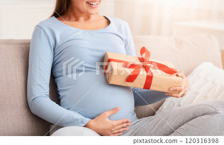 Baby Shower Gift. Pregnant Woman Holding Wrapped Box Smiling Sitting On Sofa At Home. Baby Shower Gift. Pregnant Woman Holding Wrapped Box Smiling Sitting On Sofa At Home. 120316398