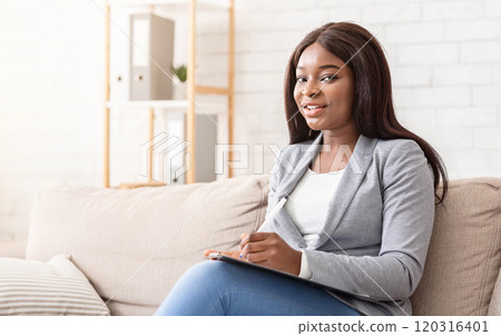 Portrait of smiling black female psychologist looking at camera and taking notes during therapy session, copy space 120316401