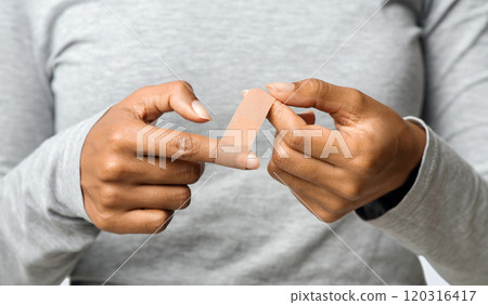 Black woman using adhesive tape on injured finger, self-treatment after trauma, close up 120316417