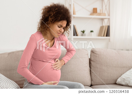 Pregnant afro woman having contraction at home, suffering from belly ache, sitting on sofa 120316438