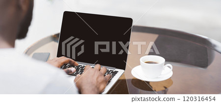 A close-up view of a mans hands typing on a laptop with a cup of coffee in the background. A close-up view of a mans hands typing on a laptop with a cup of coffee in the background. 120316454