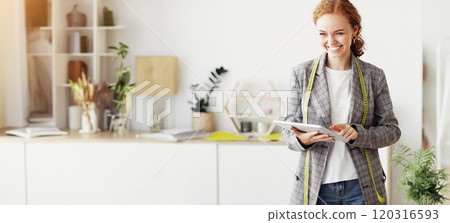 Smiling woman with measuring tape using tablet in bright design studio. 120316593
