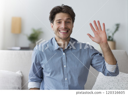 Hello. Smiling Man Waving Hand Looking At Camera Sitting On Sofa Indoor. Hello. Smiling Man Waving Hand Looking At Camera Sitting On Sofa Indoor. 120316605