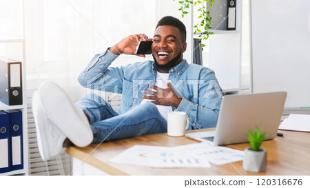 Spare time at work. Laughing employee relaxing in office, talking on phone with legs on table and drinking coffee, copy space 120316676