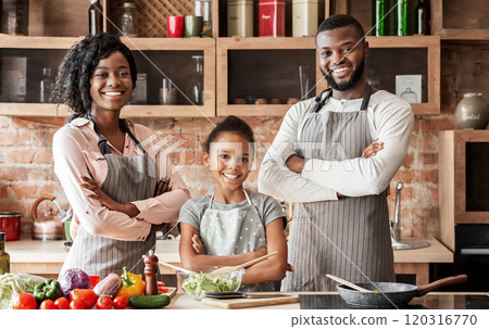 Successful cheerful african family in aprons posing over kitchen background, cooking together, free space 120316770