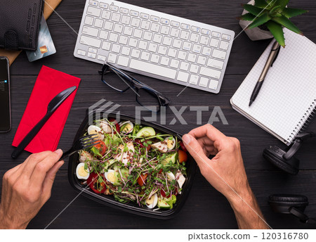 Having lunch at workplace. Businessman enjoying healthy salad at work desk, top view Having lunch at workplace. Businessman enjoying healthy salad at work desk, top view 120316780