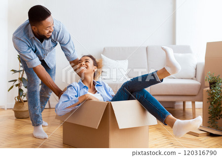 Celebrating Relocation. Happy Couple New House Owners Having Fun Riding In Moving Boxes At Home. Selective Focus Celebrating Relocation. Happy Couple New House Owners Having Fun Riding In Moving Boxes At Home. Selective Focus 120316790