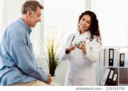 Medicine Concept. Brazilian doctor giving asthma inhaler to elderly man who's sitting on examination table, free space 120316793