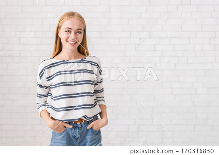 Pretty blonde girl with hands in pockets smiling over white brick wall Pretty blonde girl with hands in pockets smiling over white brick wall 120316830
