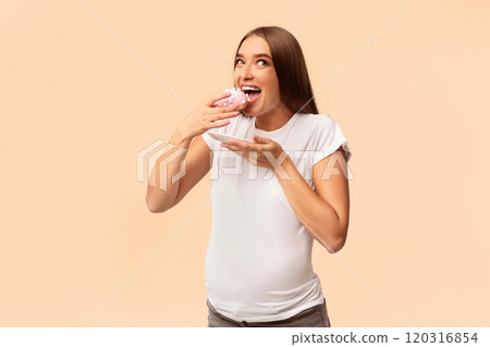 Pregnancy Nutrition. Excited Pregnant Lady Eating Unhealthy Donut Dessert Standing Over White Studio Background. Pregnancy Nutrition. Excited Pregnant Lady Eating Unhealthy Donut Dessert Standing Over White Studio Background. 120316854