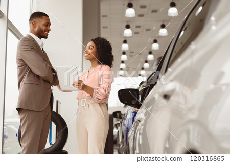Car Dealership. Auto Dealer Lady Showing Automobile To Afro Businessman Buyer Standing In Store. Copy Space Car Dealership. Auto Dealer Lady Showing Automobile To Afro Businessman Buyer Standing In Store. Copy Space 120316865
