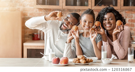 Cheerful african american family having fun during breakfast at kitchen, holding homemade cupcakes 120316867