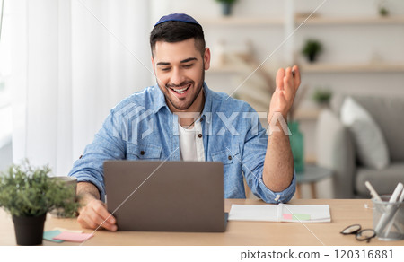 Distant Communication Concept. Portrait of happy jewish male in yarmulke and casual shirt making video call sitting at desk at home office and talking with colleagues, students or family, explaining Distant Communication Concept. Portrait of happy jewish male in yarmulke and casual shirt making video call sitting at desk at home office and talking with colleagues, students or family, explaining 120316881
