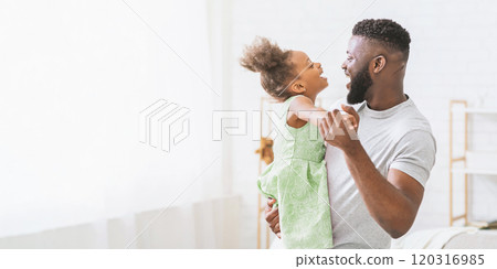A happy African American father and his daughter are dancing together in a bright and spacious living room. They two are smiling and laughing as they enjoy their playful dance, copy space A happy African American father and his daughter are dancing together in a bright and spacious living room. They two are smiling and laughing as they enjoy their playful dance, copy space 120316985