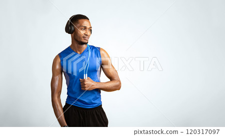 Fitness Model. Confident afro man wearing headphones and holding jumping rope on neck over yellow studio wall, copyspace 120317097