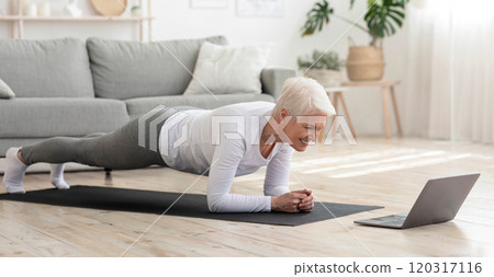 Training At Home. Sporty senior woman doing yoga plank while watching online tutorial on laptop, exercising in living room, free space, panorama Training At Home. Sporty senior woman doing yoga plank while watching online tutorial on laptop, exercising in living room, free space, panorama 120317116