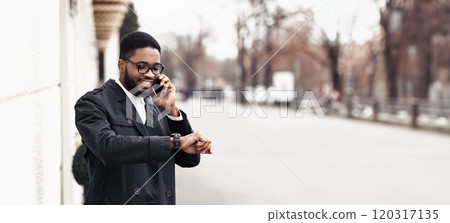 African American manager in formal outfit have phone conversation outdoors, standing by modern building on the street, checking time on watch, panorama with copy space 120317135