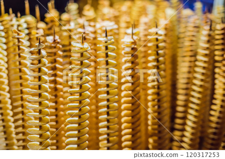 Spiral potatoes fried, on wooden sticks, spiral. Selling food at the market. Unhealthy fried food. Street food, a spiral fried potato on a stick 120317253