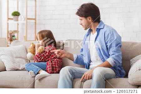 Offended little girl sitting on couch while dad scolding her for bad behaviour, home interior Offended little girl sitting on couch while dad scolding her for bad behaviour, home interior 120317271