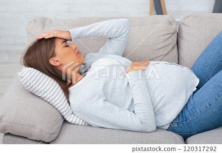 Pregnant woman feeling bad suffering from pain lying on couch at home. Sickness during pregnancy 120317292