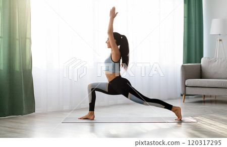 Yoga woman in sportswear exercising at home, standing in warrior pose on fitness mat, side view, copy space, full length shot. Healthy, sporty lifestyle, yoga practicing at home during self-isolation Yoga woman in sportswear exercising at home, standing in warrior pose on fitness mat, side view, copy space, full length shot. Healthy, sporty lifestyle, yoga practicing at home during self-isolation 120317295