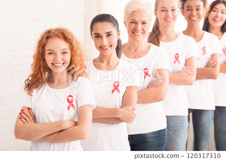 Multiethnic Ladies Volunteers In Pink Cancer Awareness T-Shirts Standing Together In Line Posing Crossing Hands On White Background. Shallow Depth Multiethnic Ladies Volunteers In Pink Cancer Awareness T-Shirts Standing Together In Line Posing Crossing Hands On White Background. Shallow Depth 120317310