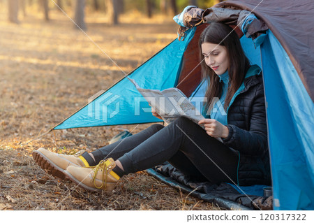 Young girl checking map in camping tent, hiking in autumn forest, empty space Young girl checking map in camping tent, hiking in autumn forest, empty space 120317322