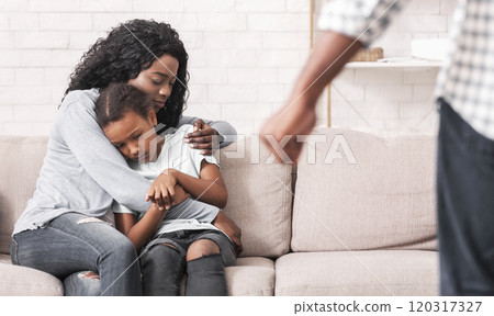 Victims of domestic violence. Afro mother and daughter suffering from home abuse, sitting on couch at home and trying to protect themselves from punch Victims of domestic violence. Afro mother and daughter suffering from home abuse, sitting on couch at home and trying to protect themselves from punch 120317327